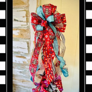 May include: A Christmas tree topper with a large red and gold bow with multiple ribbons in red, gold, black, white, and teal.