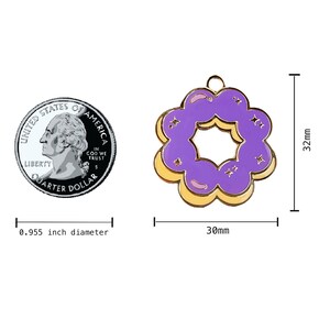 K&ouml;nnte beinhalten: Ein lila-gelber Donut-Anh&auml;nger aus Emaille mit goldener Oberfl&auml;che. Der Anh&auml;nger ist 30 mm im Durchmesser und 32 mm hoch.