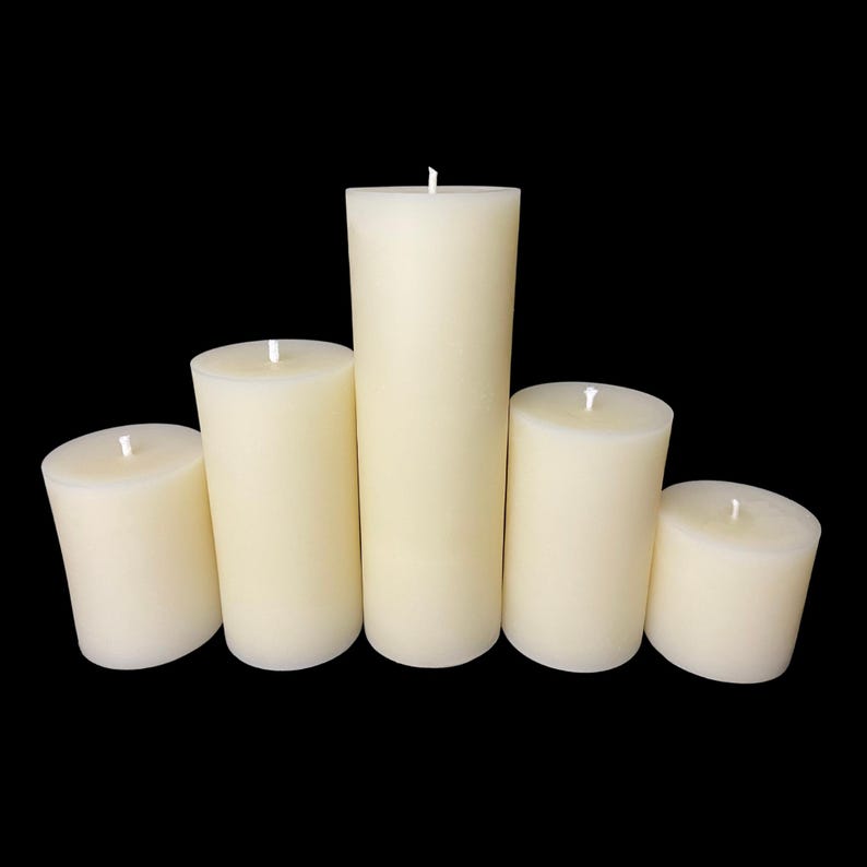 Pu&ograve; includere: Cinque candele a colonna color avorio di diverse altezze disposte su sfondo nero. Ogni candela ha uno stoppino bianco centrato sulla parte superiore piatta. Le candele sono cilindriche, con cera liscia e non profumata.