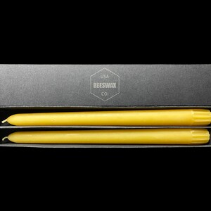 May include: Two yellow beeswax candles in a black box with the text "USA BEESWAX CO."
