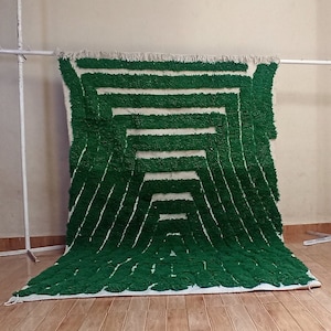 May include: A green and white geometric patterned rug with a fluffy texture. The rug is hanging on a white stand.
