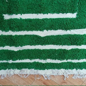 May include: A green and white rug with a geometric pattern. The rug has a fringe border.