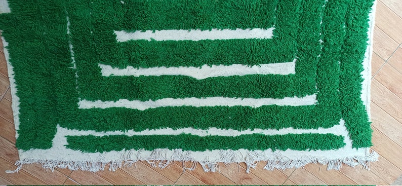 May include: A green and white rug with a geometric pattern. The rug has a fringe border.