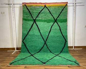 May include: A green Moroccan rug with a diamond pattern in black. The rug has a colorful border with pink, yellow, and red stripes.