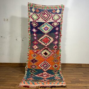 May include: A colourful Moroccan rug with a geometric pattern in shades of red, orange, green, blue, and white. The rug has a fringed edge and is made of wool.