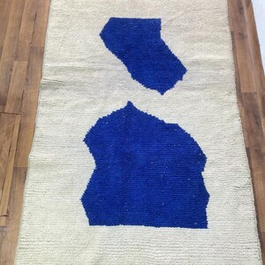 May include: A white rug with two blue abstract shapes. The rug has a fringe border.