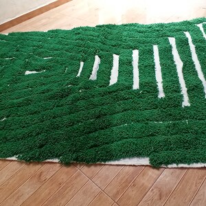 May include: A green and white rug with a geometric pattern. The rug is made of fluffy, textured yarn and has a fringe border.