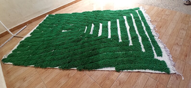 May include: A green and white rug with a geometric pattern. The rug is made of fluffy, textured yarn and has a fringe border.