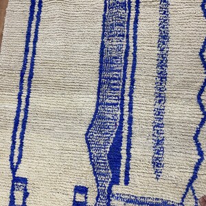 May include: A white rug with a blue geometric pattern. The pattern features a series of vertical lines and a curved shape.