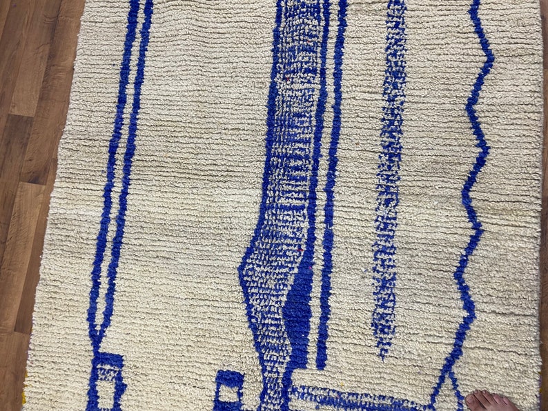 May include: A white rug with a blue geometric pattern. The pattern features a series of vertical lines and a curved shape.