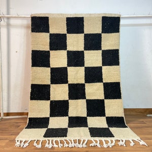May include: A black and white checkered rug with fringe on the edges. The rug is made of wool and has a traditional design.