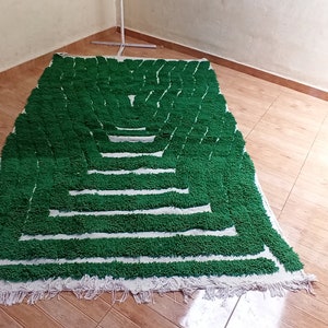 May include: A green and white rug with a geometric pattern. The rug is made of fluffy, looped yarn and has a fringe border.