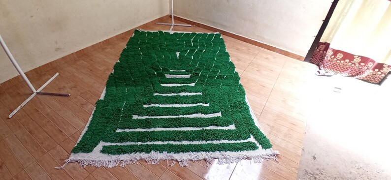 May include: A green and white rug with a geometric pattern. The rug is made of fluffy, looped yarn and has a fringe border.