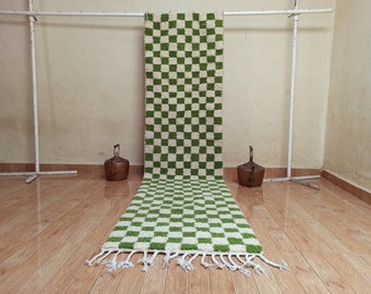 May include: A green and white checkered rug with a fringe border. The rug is hanging on a white metal rack.