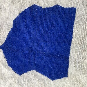 May include: A white rug with a blue abstract design. The rug has a fringe border.