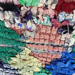 Puede incluir: Primer plano de una alfombra colorida y texturizada hecha con retazos de tela reciclados. La alfombra presenta una variedad de colores, incluyendo verde, azul, rosa y amarillo. Los retazos de tela est&aacute;n tejidos juntos para crear un patr&oacute;n &uacute;nico e interesante.