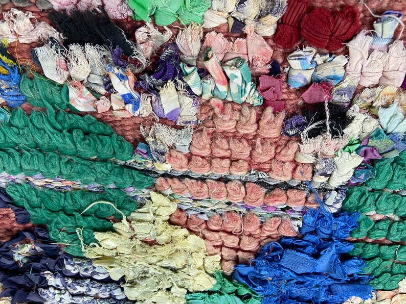 Puede incluir: Primer plano de una alfombra colorida y texturizada hecha con retazos de tela reciclados. La alfombra presenta una variedad de colores, incluyendo verde, azul, rosa y amarillo. Los retazos de tela est&aacute;n tejidos juntos para crear un patr&oacute;n &uacute;nico e interesante.
