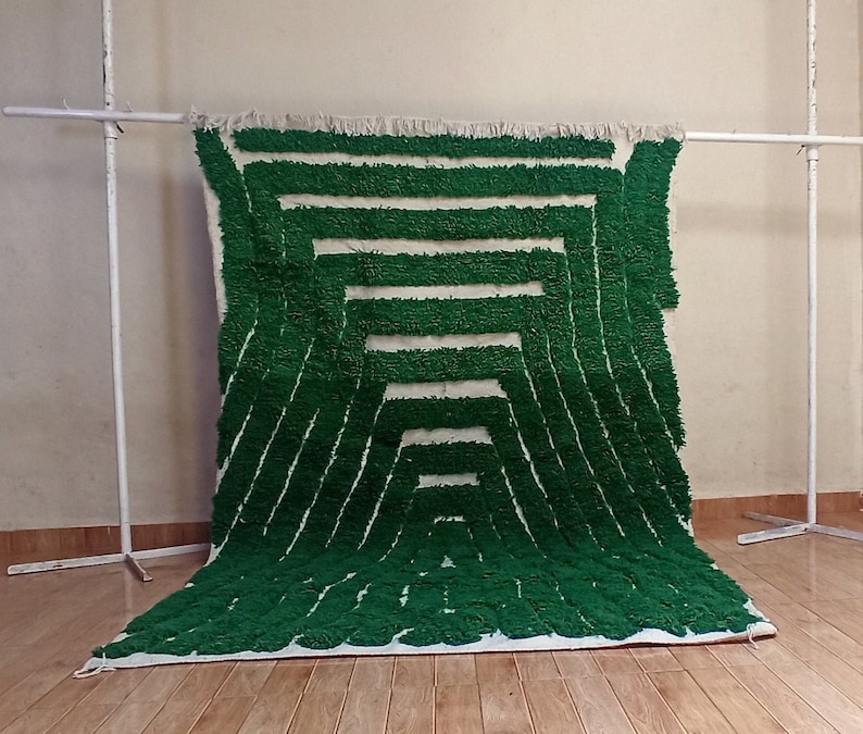 May include: A green and white geometric patterned rug with a fluffy texture. The rug is hanging on a white stand.