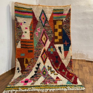 May include: A colorful Moroccan rug with geometric patterns in shades of red, orange, blue, green, and pink. The rug has a white background and is woven with a variety of textures.