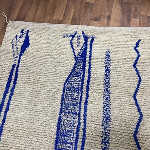 May include: A white rug with a blue geometric pattern. The pattern features three vertical lines with a wavy design on the right side.
