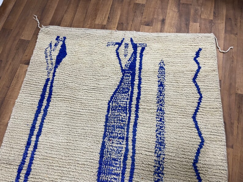 May include: A white rug with a blue geometric pattern. The pattern features three vertical lines with a wavy design on the right side.
