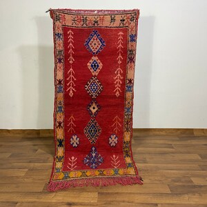 May include: A red, blue and yellow patterned rug with fringe. The rug has a geometric design with diamonds and other shapes.