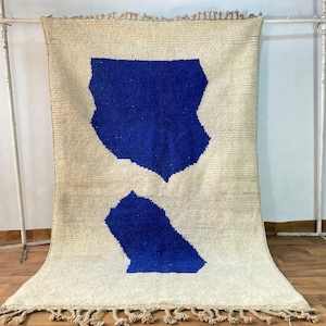 May include: A white rug with two blue abstract shapes. The rug has fringe on the bottom edge.