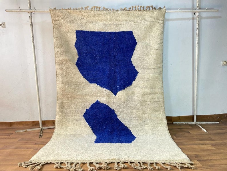 May include: A white rug with two blue abstract shapes. The rug has fringe on the bottom edge.