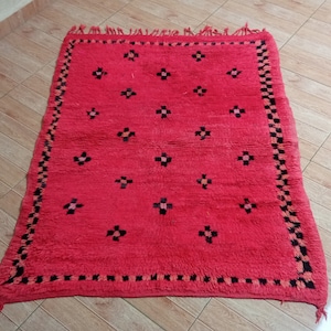 May include: A red Moroccan rug with a black and white geometric pattern. The rug has a fringe border.