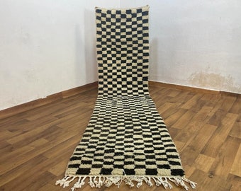 May include: A black and white checkered rug with a fringe border. The rug is made of wool and has a traditional Moroccan design.
