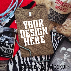 Könnte beinhalten: Ein braunes T-Shirt mit Leopardenmuster und dem weißen Text "YOUR DESIGN HERE". Das Bild enthält einen Hut mit Leopardenmuster und dem Text "EXPENSIVE & DIFFICULT", ein Buch und ein gerahmtes Bild.
