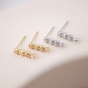 May include: Three pairs of earring findings with a row of three clear cubic zirconia stones. The findings are available in gold and silver.