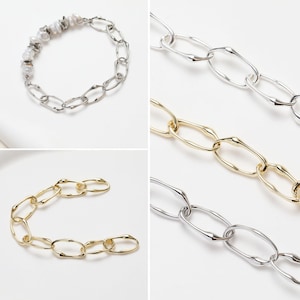 Puede incluir: Tres collares de cadena de plata y oro con eslabones ovalados irregulares. La cadena de plata es un collar con un adorno de perlas y cuentas de plata. La cadena de oro es un collar más corto con eslabones más grandes. La cadena de plata es un collar más largo con eslabones más pequeños.