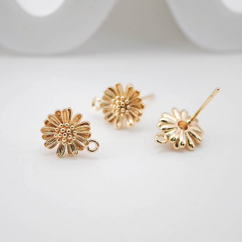 May include: Three gold-toned daisy flower earring findings with a loop on one side and a post on the other.