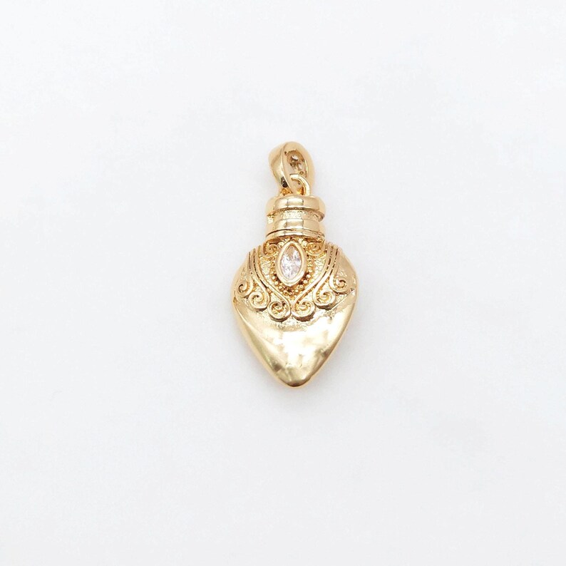 May include: A gold-tone pendant shaped like a heart-shaped bottle with an ornate design and a clear rhinestone in the center.
