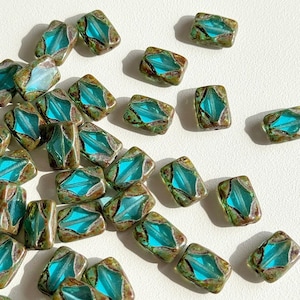 Peut inclure: Un ensemble de perles de verre rectangulaires avec un centre turquoise et une couche extérieure marron et verte. Les perles présentent un motif en forme de losange au centre. Ces perles sont adaptées à la fabrication de bijoux.