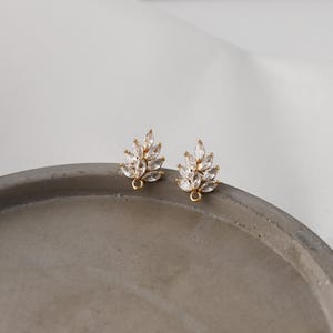 May include: A pair of gold-toned earring components shaped like leaves, each featuring multiple marquise-cut clear cubic zirconia stones arranged in a cluster. Each piece includes a small circular loop at the base for attaching additional jewelry elements.