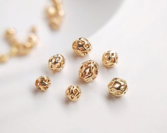 Peut inclure: Un ensemble de huit perles en métal de couleur dorée avec un design délicat et ajouré. Les perles sont éparpillées sur une surface blanche.