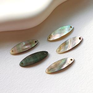 Może przedstawiać: Pięć owalnych zawieszek z perłowej muszli z otworem na każdym końcu. Zawieszki są opalizujące w odcieniach zieleni, brązu i bieli.