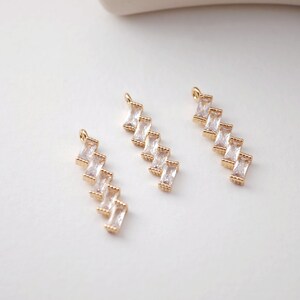 May include: Three gold-toned pendant charms with a staggered design of five clear rectangular crystals.