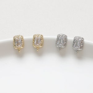 Puede incluir: Dos pares de cierres de pendientes con una piedra rectangular transparente engastada en un marco dorado o plateado. Los cierres tienen un pequeño bucle para sujetar una cadena u otras joyas.