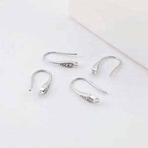May include: Four silver earring hooks with clear crystal accents. The hooks are designed to be used for making earrings.