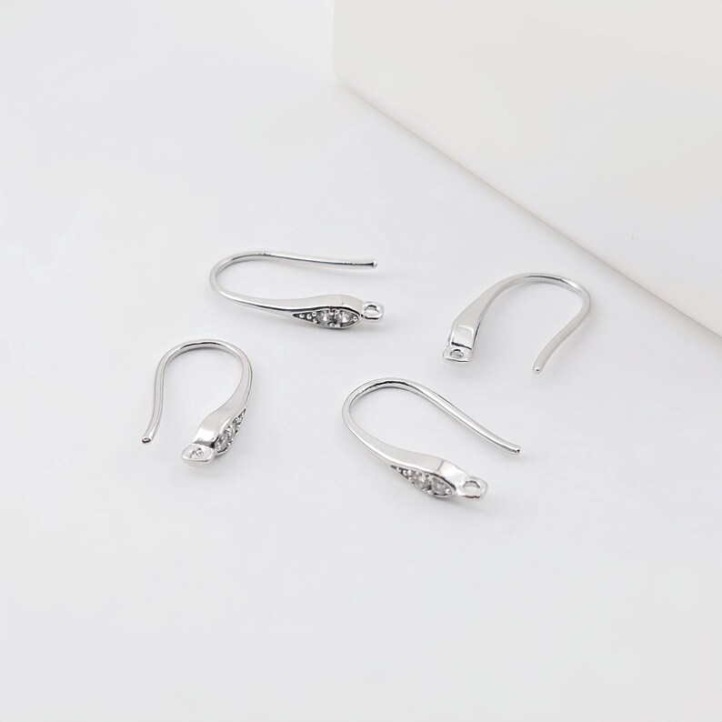 May include: Four silver earring hooks with clear crystal accents. The hooks are designed to be used for making earrings.