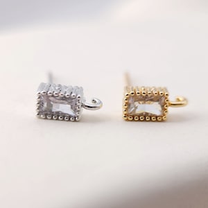 May include: Two small rectangular earrings with clear stones set in a gold and silver frame. The earrings have a small hook closure.