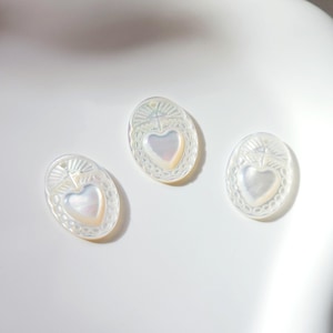 Peut inclure: Trois breloques ovales en nacre blanche avec un motif de cœur en relief et une croix en haut.