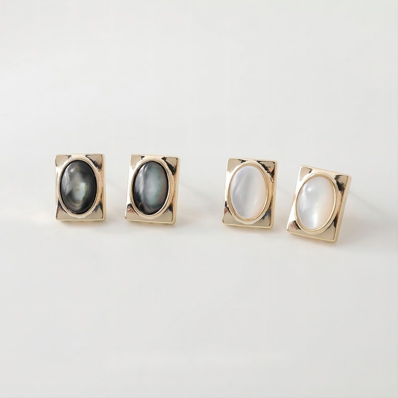 May include: A set of four gold-toned earrings with oval-shaped mother-of-pearl stones. Two earrings have black stones and two earrings have white stones.