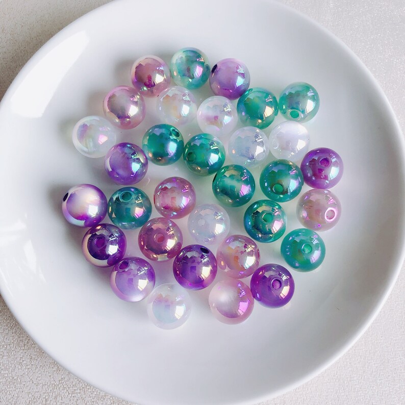 May include: A collection of iridescent glass beads in shades of purple, teal, and white. The beads are round and have a smooth, glossy finish.