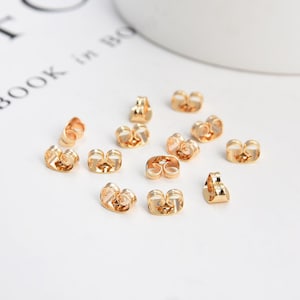 May include: A close-up of a group of gold-colored earring backs. The backs are designed to help keep earrings in place.