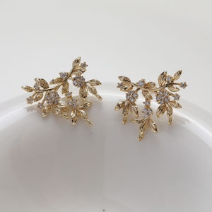 May include: A pair of gold earrings with a delicate floral design. The earrings feature small, clear crystals that add sparkle and shine.