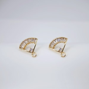 Könnte beinhalten: Ein Paar goldfarbene Ohrring-Verschlüsse mit einem fächerförmigen Design. Der Fächer ist mit klaren Zirkonia-Steinen verziert. Die Verschlüsse haben eine Schlaufe unten zum Anbringen von Ohrringen.